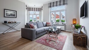 En moderne stue med en grå sofa, et glasterbord og et rødt tæppe med mønster.