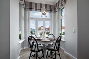 Ein Essbereich mit einem weißen Tisch, gedeckt für vier Personen, schwarzen Stühlen, einer Chandelier und Blick auf Gebäude durch große Fenster.
