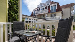 En balkon med to stole og et bord, med udsigt over en bygning med flere balkoner og et rødt tegltag.