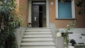 A building entrance with a concrete staircase leading to a door, a window with a blue shutter, and potted plants. - R&B La Villa (Bologna)