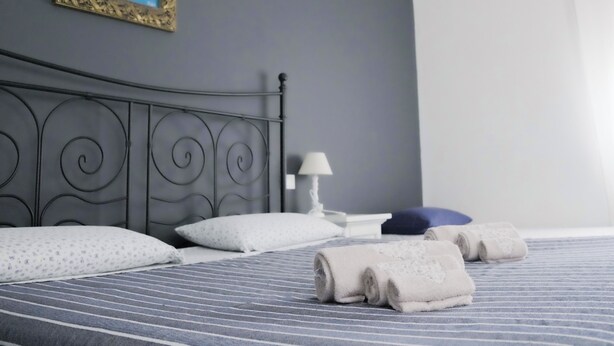 A neatly made bed with striped bedding, a headboard, pillows, a lamp, and towels on a blue-striped bedspread. - R&B La Villa (Bologna)