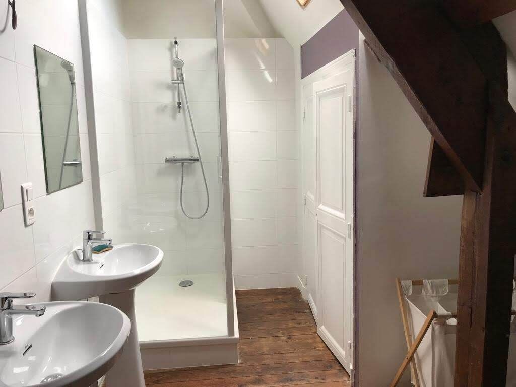A bathroom with a glass shower enclosure, two sinks, and a wooden floor.