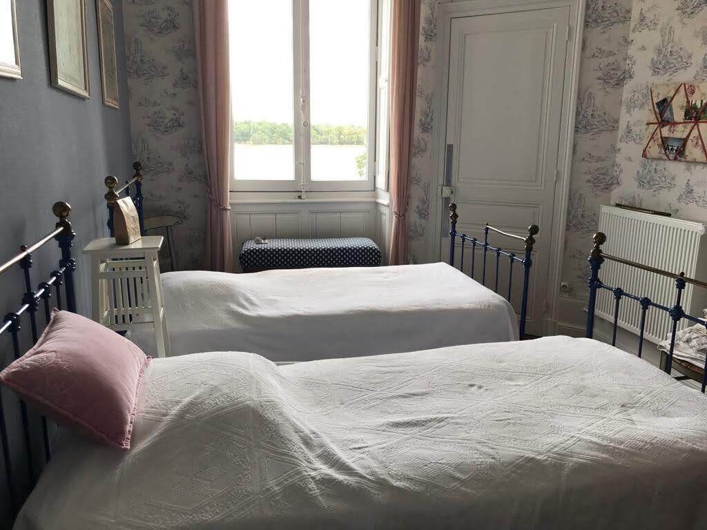 A bedroom with two beds, a window with curtains, a radiator, and a wall with a floral pattern.