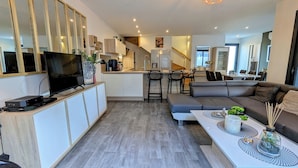 A modern living room with a large TV, a sofa, and a dining area with bar stools. - NEAR PINARELLO BEACH - LUXURY VILLA FOR 9 PEOPLE - AIR-CONDITIONED WITH SWIMMING POOL (Sainte-Lucie de Porto-Vecchio)
