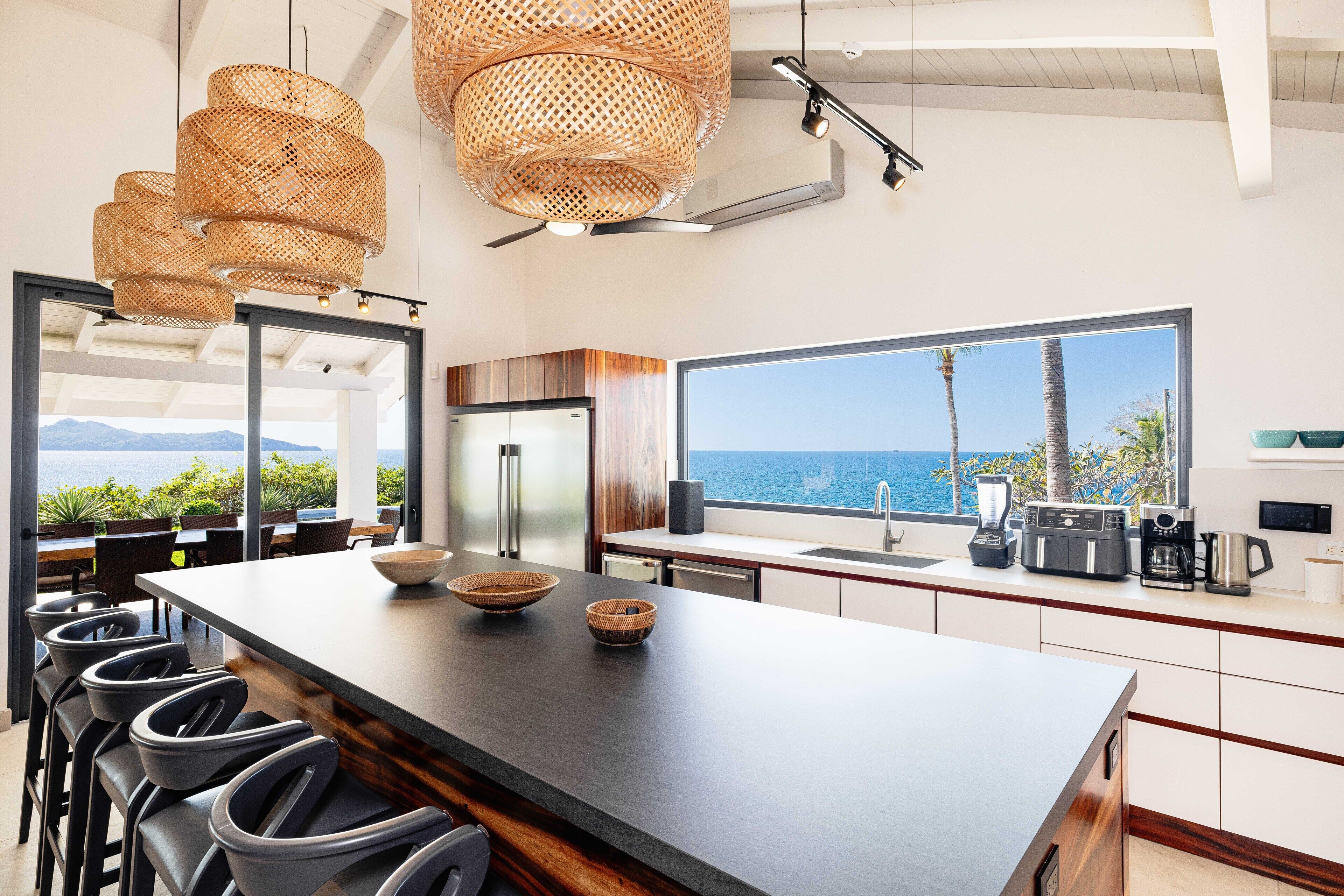 Une cuisine moderne dotée d’un grand îlot central, de tabourets de bar et offrant une vue sur la mer.