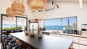 A modern kitchen with a large island, bar stools, and a view of the sea. - Beachfront Cliff Villa • 300° Ocean Views • Pool, Jacuzzi & Guest House (Playa Flamingo)