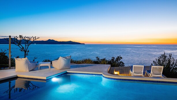 A poolside area with lounge chairs and a view of the sea at sunset. - Beachfront Cliff Villa • 300° Ocean Views • Pool, Jacuzzi & Guest House (Playa Flamingo)