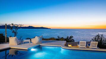 Un espace aménagé au bord de la piscine, avec des chaises longues et une vue sur la mer au coucher du soleil.