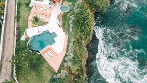 An aerial view of a coastal property with a swimming pool, outdoor seating, and a view of the ocean. - Beachfront Cliff Villa • 300° Ocean Views • Pool, Jacuzzi & Guest House (Playa Flamingo)