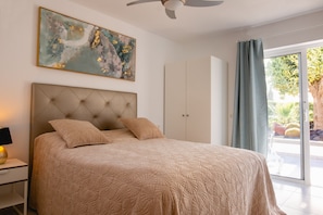 A bedroom with a tufted headboard, a large abstract painting, a wardrobe, and a view of the outdoors.