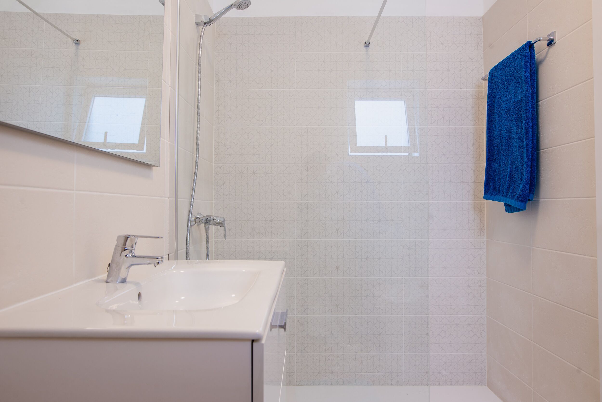 A bathroom with a white sink, a mirror, a shower, and a blue towel on the wall.