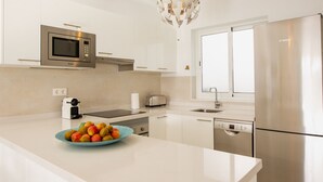A modern kitchen with white cabinetry, a stainless steel refrigerator, a microwave, a toaster, and a bowl of fruit on the counter.