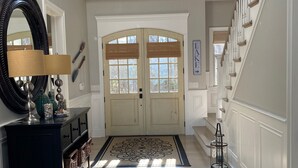 A spacious entryway with a large mirror, a dark wooden console, and a decorative rug leading to a staircase. - Southampton  PRIVATE Waterfront Estate!
 (Hampton Bays)