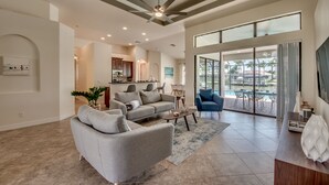 A spacious living area with a grey sofa, a coffee table, and a ceiling fan. There is a kitchen in the background and a large sliding glass door leading to an outdoor patio. - Villa Destiny, great villa with modern ambience, pool and spa facing south (Cape Coral)