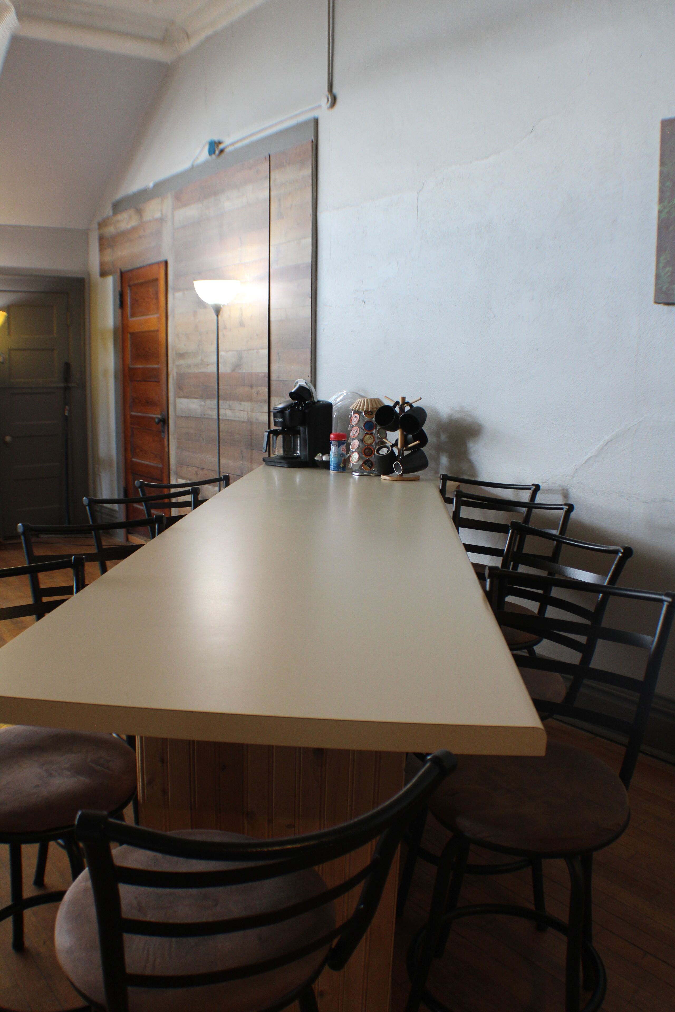 Una larga mesa de comedor con sillas, una cafetera y una lámpara sobre la mesa.