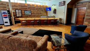 A bar area with a wooden counter, bar stools, a TV mounted on the wall, and a refrigerator with a Pepsi logo. - 3BR on SXS Snowmobile Trail w/Full Bar, Walk to Dining &Bars, Near MTU &Houghton (South Range)