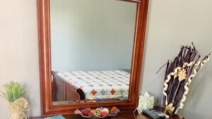 A wooden dresser with a large mirror, a bed with a patterned bedspread, a small plant, and decorative items. - Apartment in Rincon (Rincon)