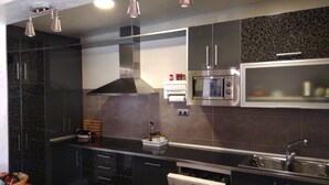 A modern kitchen with black cabinets, a stainless steel range hood, a microwave, and a dishwasher. - Hobbit House (bioclimatic and half-buried with green cover). (Alba de los Cardaños)
