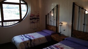 A room with two beds, a window with a view of a landscape, a wall-mounted lamp, and a curtain. - Hobbit House (bioclimatic and half-buried with green cover). (Alba de los Cardaños)