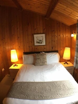 A wooden-paneled room with a bed, two bedside lamps, and a framed picture on the wall.