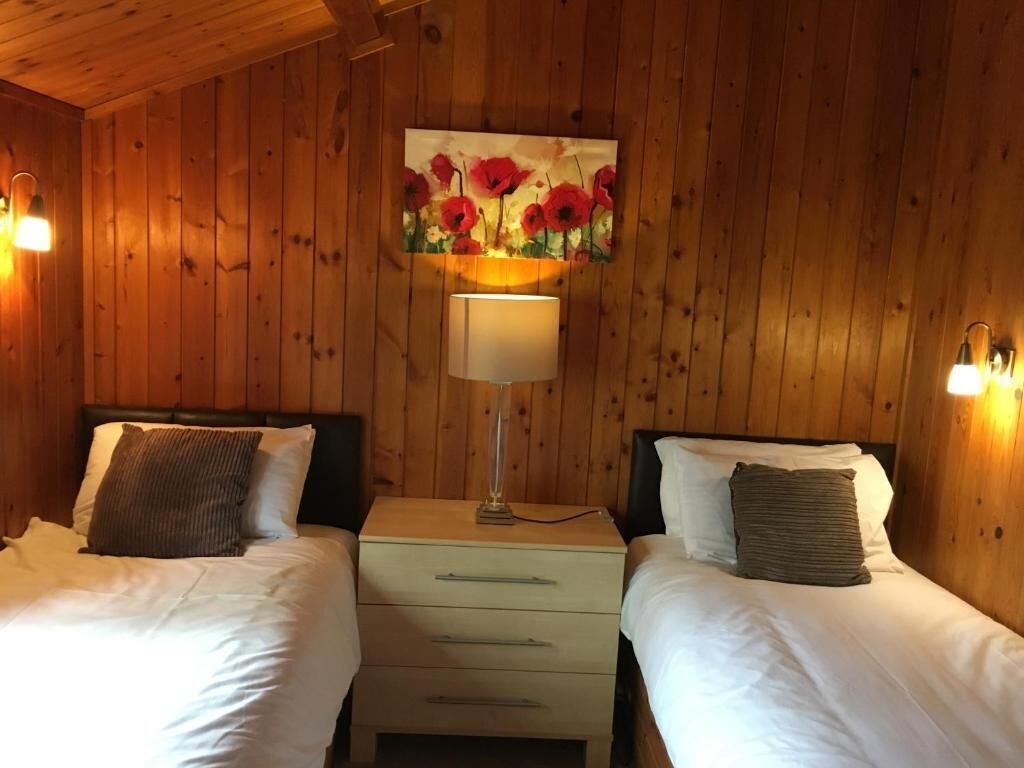 A wooden-paneled room with two beds, each with white bedding and a lamp between them.
