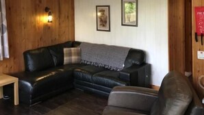 A wooden interior with a black leather sofa, a ceiling fan, and a mounted deer skull.