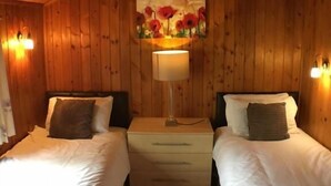A wooden room with two beds, a nightstand with a lamp, and a painting on the wall.