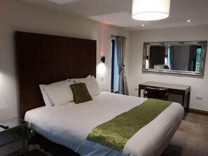 A hotel room with a large bed, a desk, a mirror, and a window with curtains. - Bluestone Hot Tub (Carmarthen)