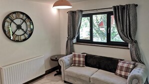 Ein Wohnzimmer mit Sofa, einer großen Wanduhr, einem Fenster mit Vorhängen und einer Heizung.