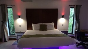 Ein Schlafzimmer mit einem großen Bett, zwei Nachttischen, einem Sessel und einem Fenster mit Vorhängen.
