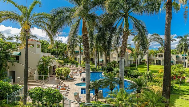 Ein Resort mit einem zentral gelegenen Pool, Palmen und einem gepflegten Rasen.