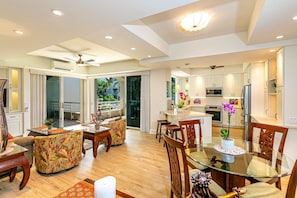 A modern kitchen with stainless steel appliances, a dining area with a glass table, and a balcony with a view of greenery. - Romantic, Luxury Maui Getaway with Ocean View - Couples Only (Kihei)