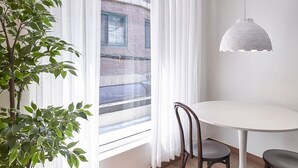 A dining area with a round table, two chairs, a hanging pendant light, and a window with sheer curtains. - Futon Guesthouse (Seoul)