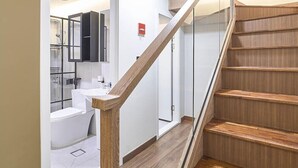 A staircase with wooden steps and glass railings leading to a bathroom with a white sink and a mirror. - Futon Guesthouse (Seoul)