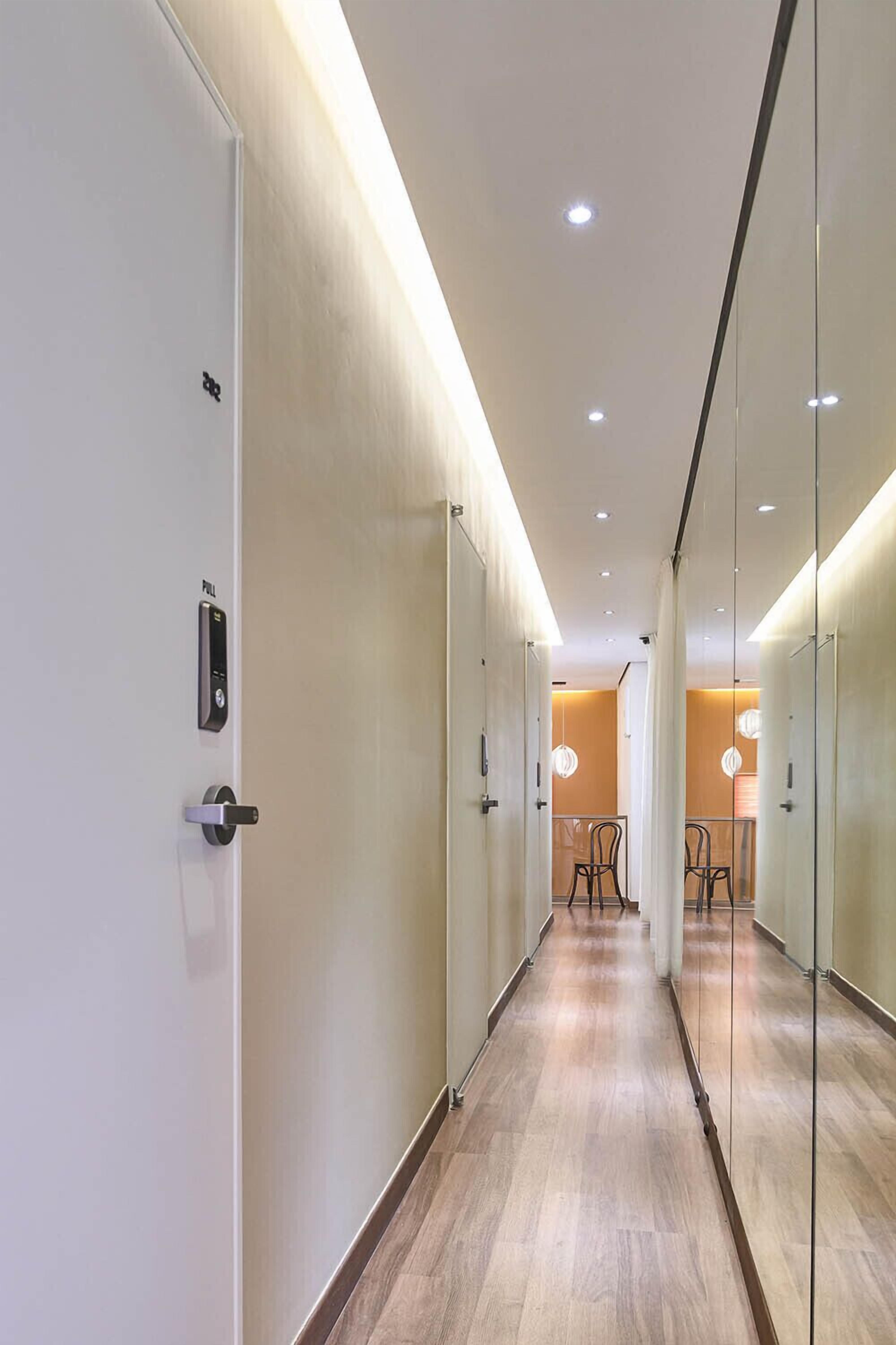 A modern hallway with glass doors, wooden flooring, and recessed lighting.