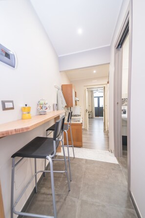 A narrow hallway with a wooden counter, two black chairs, and a yellow appliance. A door leads to a balcony.