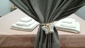 A room with a bed covered in a pink bedspread, a gray curtain tied with a checkered cloth, and two stacks of white towels on the bed. - Central Station House Riccardo (Catania)