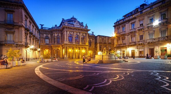 A historic building with ornate architecture, a central fountain, and a cobblestone plaza.