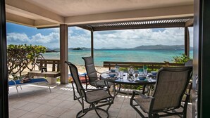 A covered outdoor seating area with a table and chairs, overlooking a beach and turquoise sea. - Sapphire Beach Resort Rental (St Thomas)