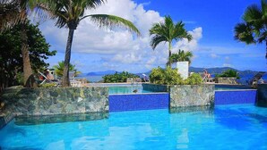 A clear blue pool with stone walls and palm trees, surrounded by lounge chairs and a view of the ocean. - Sapphire Beach Resort Rental (St Thomas)
