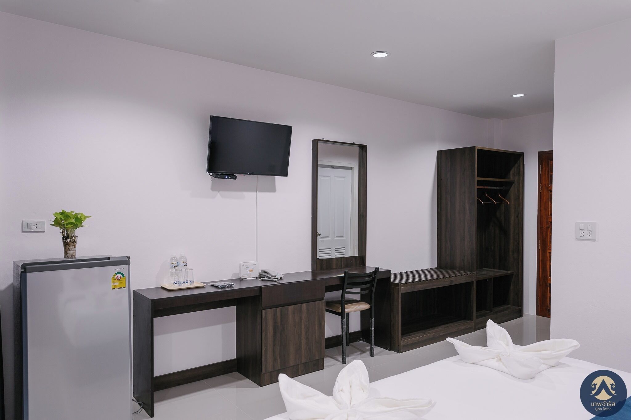Een moderne hotelkamer met een bureau, stoel, televisie, kast en een bed met handdoeken.