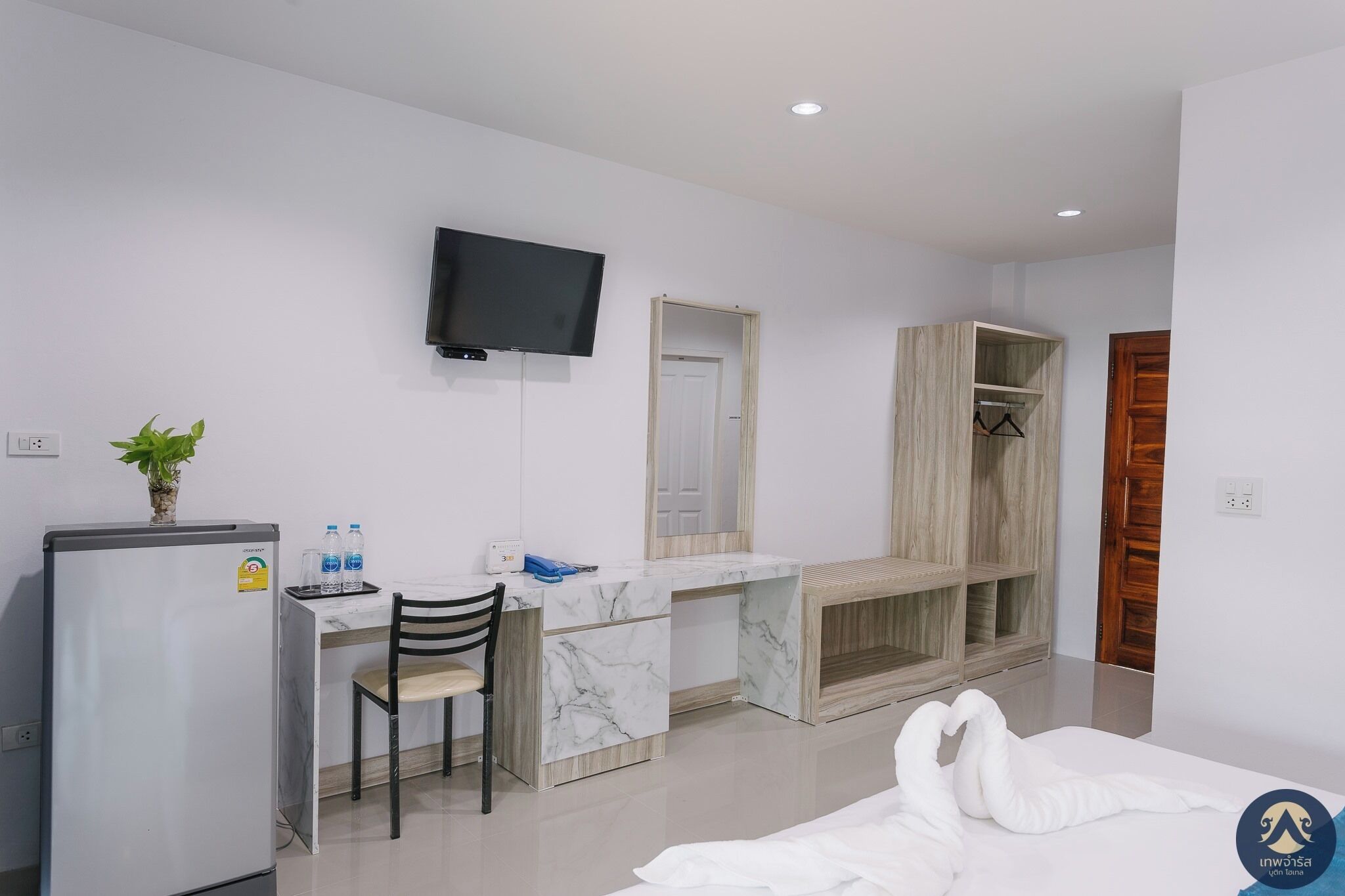 A modern hotel room with a marble desk, a flat-screen TV, a wardrobe, and a bed with a white swan decoration.
