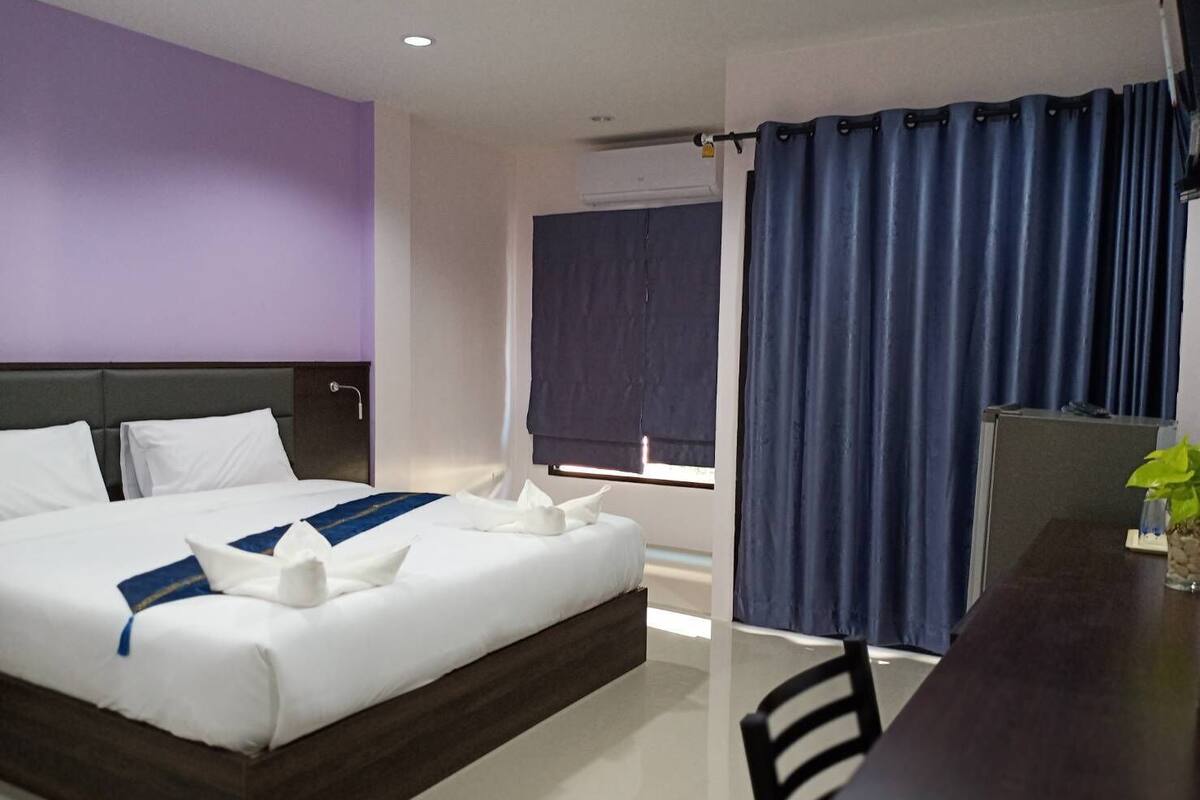 Une chambre d’hôtel avec un lit, un bureau, une chaise, une fenêtre avec des rideaux et une plante sur le bureau.