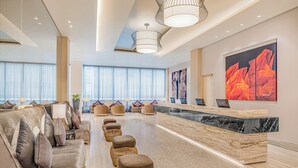 A modern hotel lobby with a reception desk, seating area, and large windows.