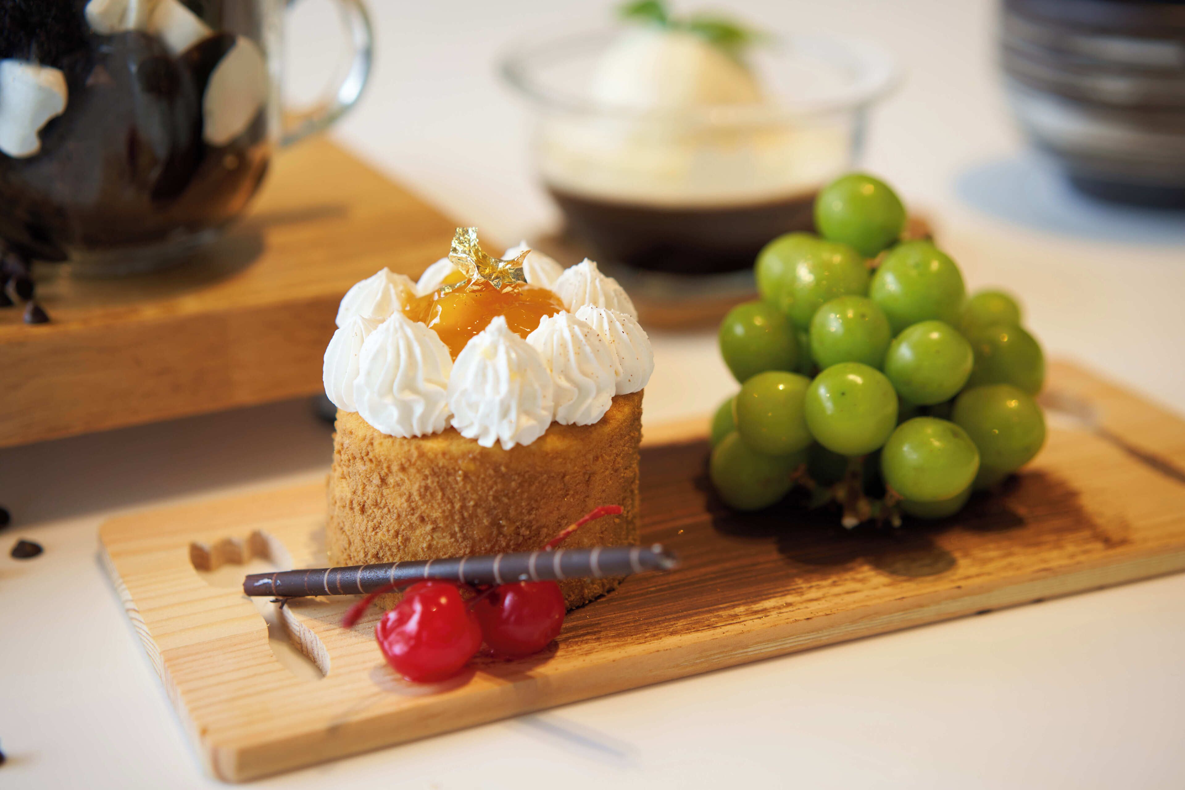 A dessert on a wooden board with whipped cream, cherries, and a chocolate stick.