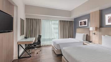 Habitación de hotel con dos camas, un escritorio, una silla, un televisor y una ventana con cortinas.