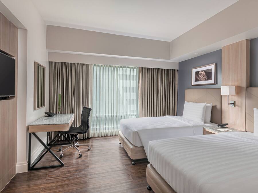 Habitación de hotel con dos camas, un escritorio, una silla, un televisor y una ventana con cortinas.