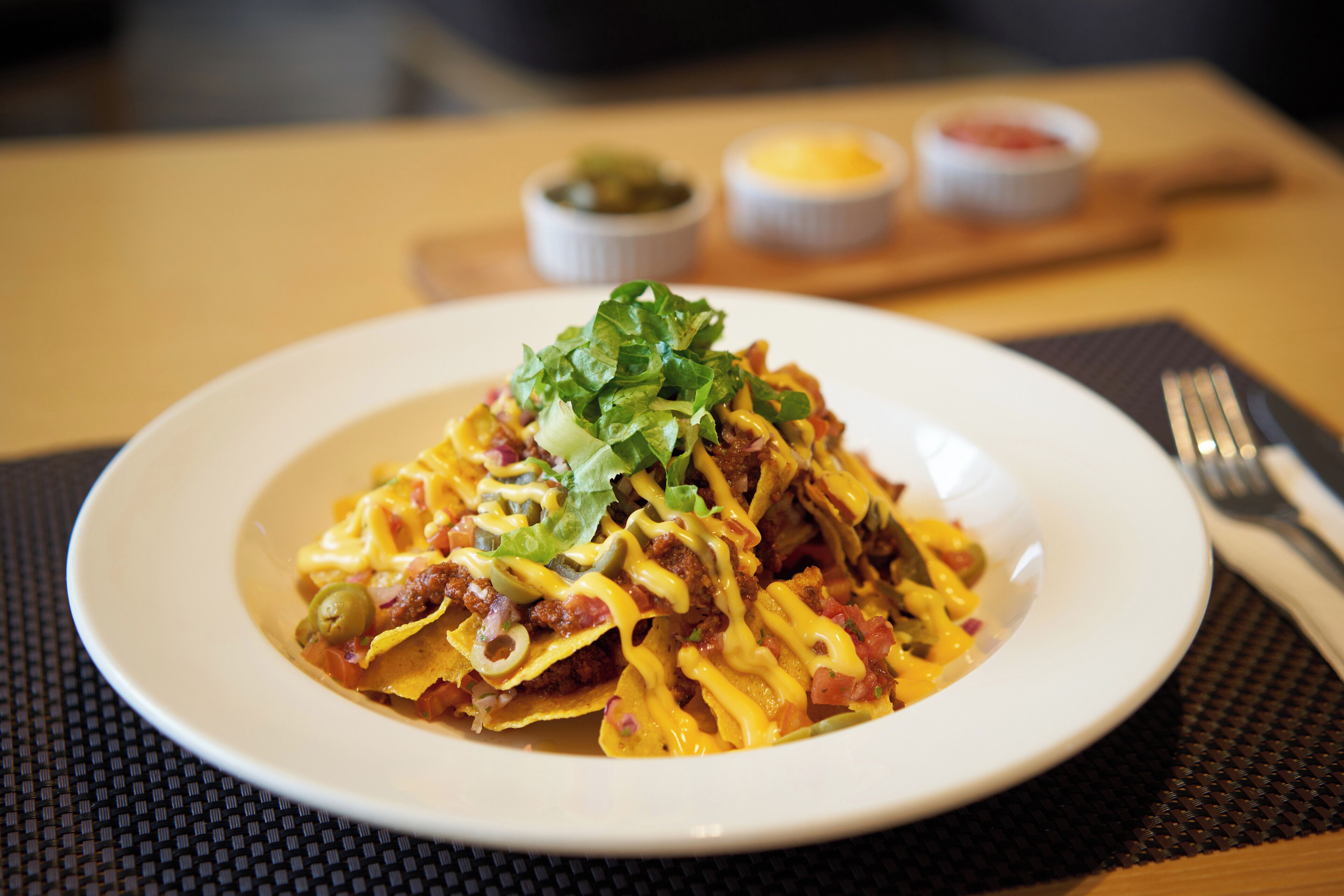 Un plato de nachos con ingredientes y salsas sobre una mesa con posavasos.