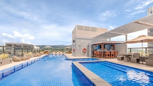 A rooftop pool with clear blue water, surrounded by lounge chairs and a bar area.