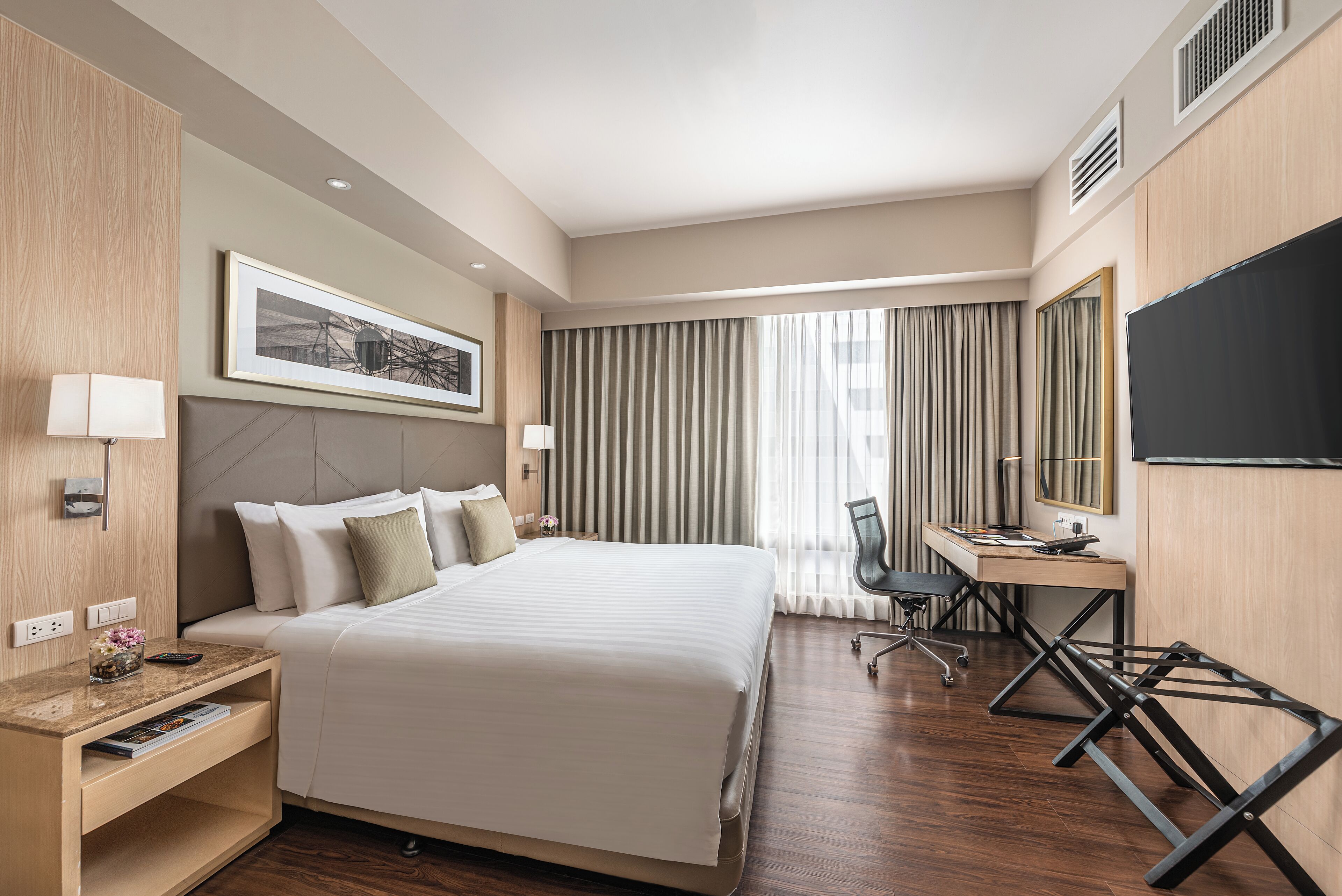 A modern hotel room with a large bed, a desk, a chair, and a television.